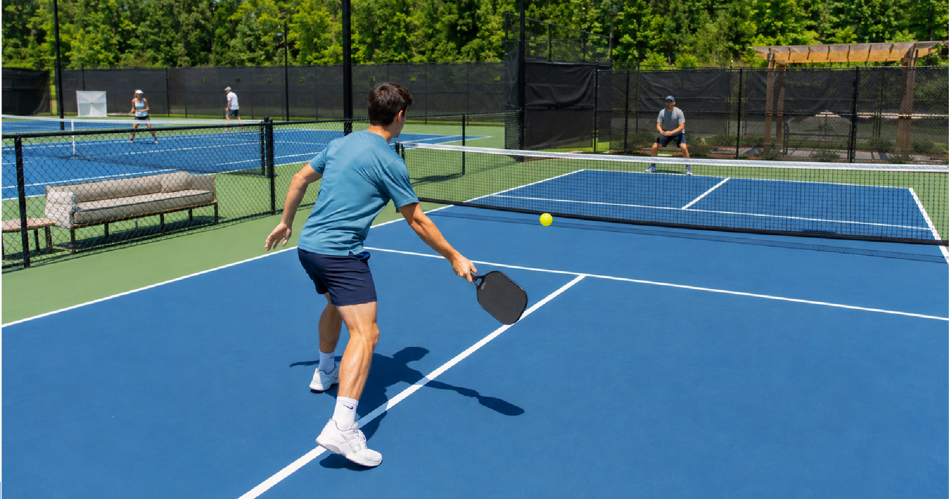Tennis player on a pickleball court holding a paddle near the kitchen line with a tennis court behind